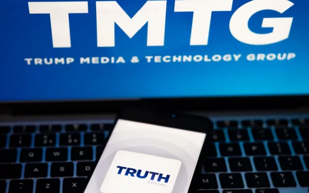 Truth Social app logo seen on the smartphone and blurred TMTG logo on the laptop.