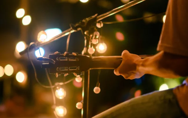 Rear view of the man sitting play acoustic guitar on the outdoor concert with a microphone stand in the front